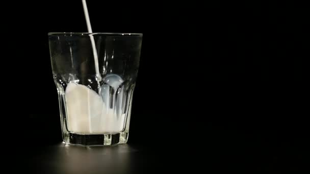 Ρίχνει γάλα σε μακρύ ρεύμα στο ένα ποτήρι σε μαύρο φόντο — Αρχείο Βίντεο