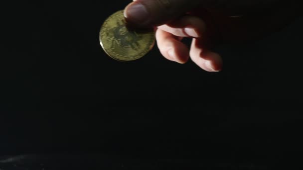 Hombre tiene en la mano un bitcoin de oro sobre fondo negro — Vídeo de stock