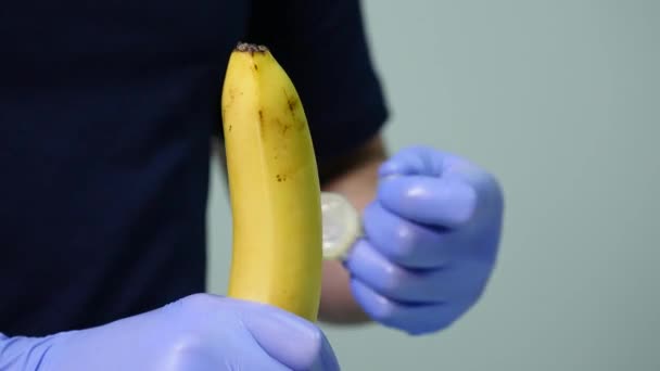 Uma mão de homem a pôr um preservativo numa banana. O conceito de sexo seguro e prevenção de doenças sexualmente transmissíveis — Vídeo de Stock