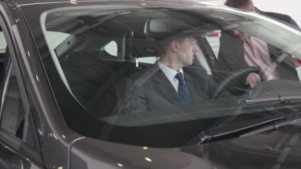 Un hombre inspecciona el interior del vehículo. Auto negocio, venta de coches, la tecnología y el concepto de la gente - macho feliz con concesionario de automóviles en el salón de exposición o auto. Joven con un vendedor en un espectáculo de motor — Vídeos de Stock