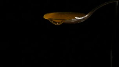 Siyah arka plan karşı kaşık akan bal