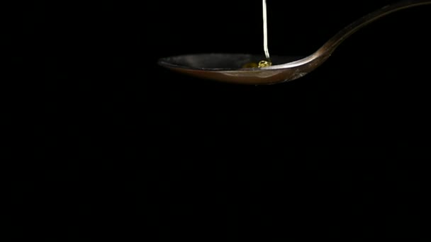 Honig tropft aus dem rostfreien Teelöffel auf schwarzem Hintergrund — Stockvideo