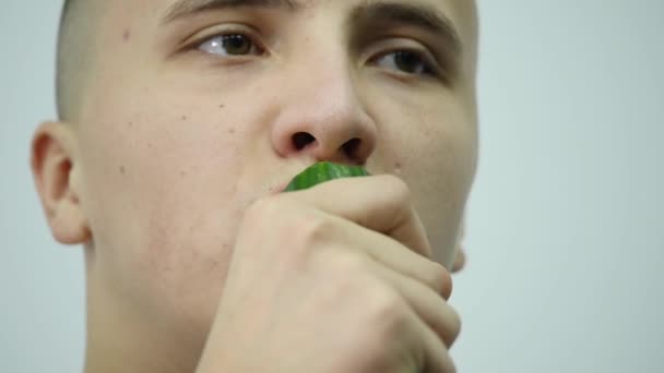 Joven comiendo un pepino sobre un fondo blanco — Vídeo de stock