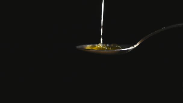 Honey dripping from the stainless tea spoon on black background — Stock Video