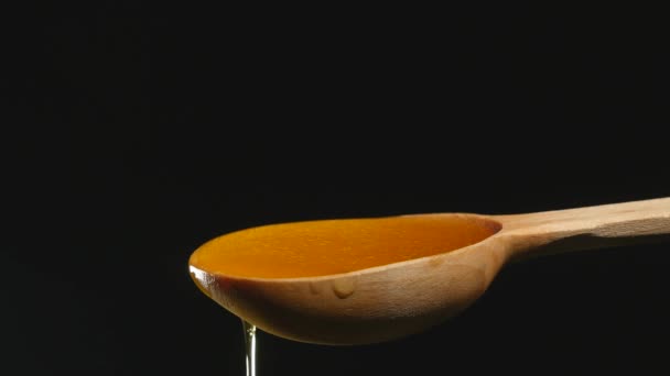 Miel goteando de una cuchara de madera sobre fondo negro — Vídeos de Stock