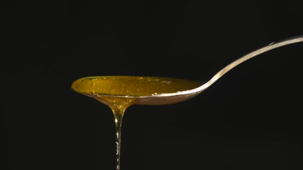 Miel fluyendo de cuchara contra fondo negro — Vídeo de stock