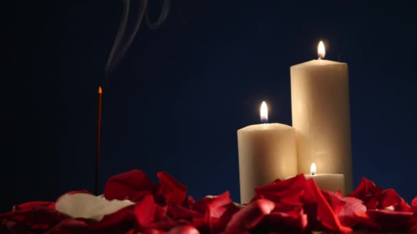 De stokken van de wierook en kaarsen met rozenblaadjes op donkere achtergrond — Stockvideo