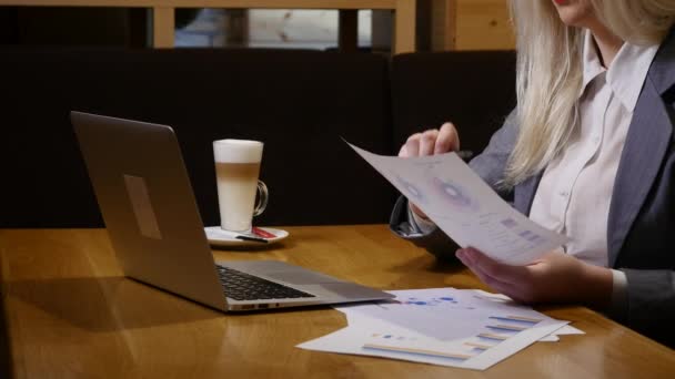 Ung affärskvinna arbetar med laptop och dokument i café — Stockvideo