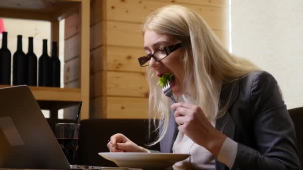 Бізнес-леді їсть обід і працює на ноутбуці в кафе — стокове відео
