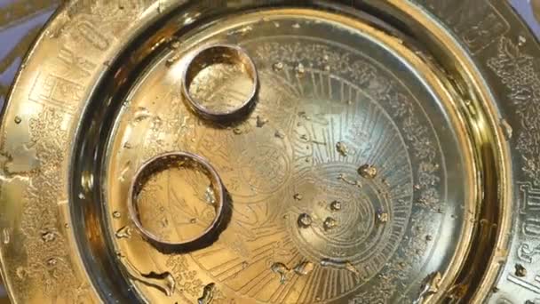 Close up of wedding rings of newlyweds during the consecration of holy water in the church before the wedding ceremony — Stock Video