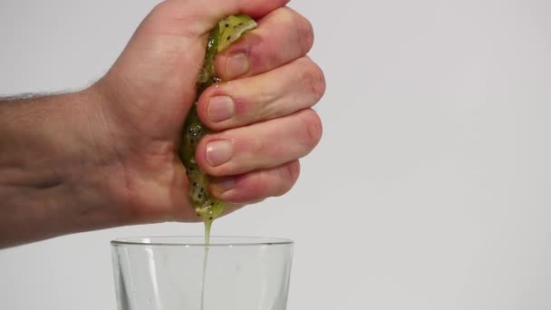 Mano exprime el jugo del kiwi en un vaso sobre un fondo blanco — Vídeo de stock