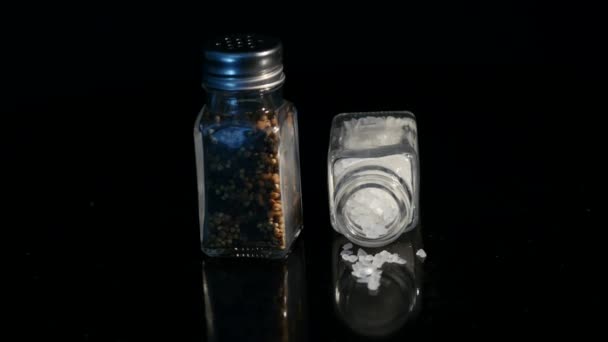 Zeezout en zwarte peper in glazen potten op zwarte achtergrondkleur weergegeven — Stockvideo