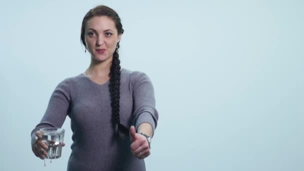 Μια νεαρή γυναίκα κρατά ένα ποτήρι νερό και δείχνει τον αντίχειρα σε λευκό φόντο — Αρχείο Βίντεο