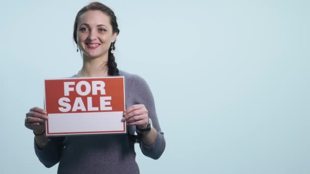 Leende kvinna som håller vit skylt styrelsen till salu — Stockvideo