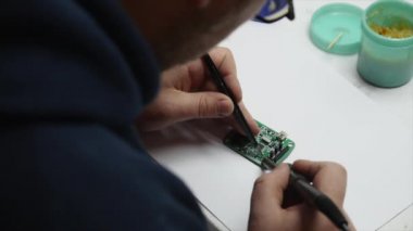 Adam lamba güç kaynağı onarıyor. Halen bir elektronik Pano ve bir havya tutuyor. Üstten Görünüm.