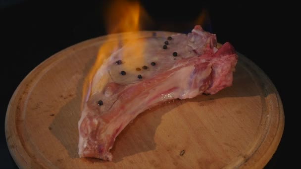 Nahaufnahme eines rohen Fleischstücks im Feuer, das sich auf einem Schneidebrett dreht — Stockvideo