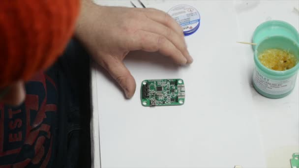 De man is het repareren van de voedingsspanning van de lamp. Hij houdt een elektronische board en een soldeerbout. Bovenaanzicht. — Stockvideo