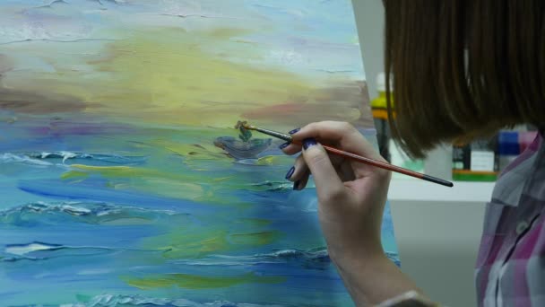 Eine junge Frau malt in einer stimmungsvollen Werkstatt hinter einer Staffelei ein Gemälde auf eine Leinwand — Stockvideo