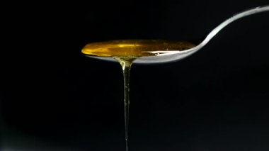 Siyah arka plan karşı kaşık akan bal
