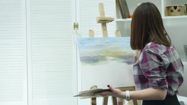 ศิลปินหญิงสาวในผ้ากันเปื้อนภาพวาดบนผ้าใบในสตูดิโอศิลปะ — วีดีโอสต็อก