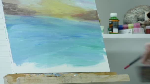 Uma jovem pinta uma pintura em uma tela, em pé atrás de um cavalete, em uma oficina atmosférica — Vídeo de Stock
