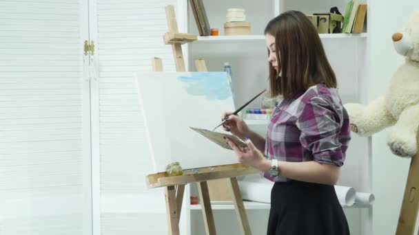 The artist comes to the picture and begins to paints oil in a bright studio. Creative male artist drawing picture with oil paints in studio — Stock Video