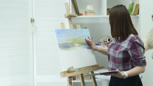 Молода жінка-художник в фартуху картина на полотні в художній студії — стокове відео