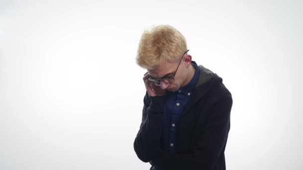 Triste joven en gafas sobre el fondo blanco — Vídeos de Stock