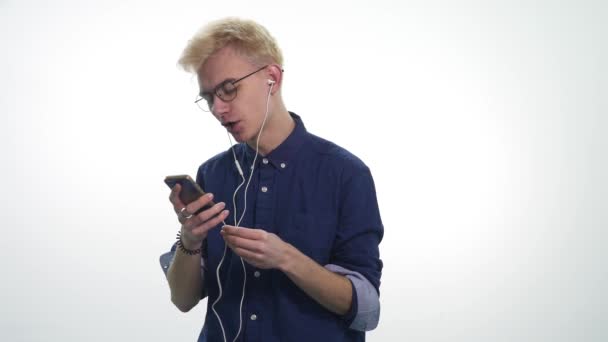 Jovem homem bonito cantando, dançando, ouvindo música em fones de ouvido sobre fundo branco — Vídeo de Stock