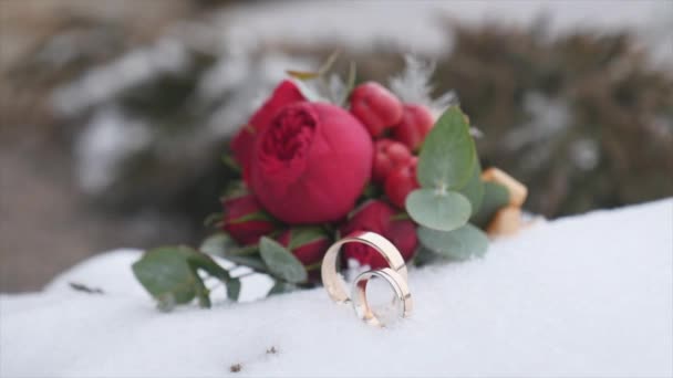 Ramo de boda con anillos de boda con flores rojas en el fondo de la nieve — Vídeos de Stock