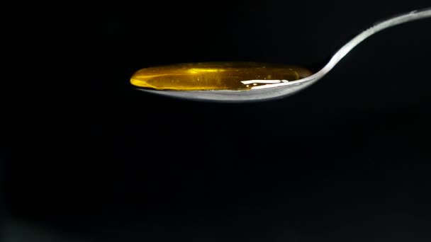 Honig fließt aus dem Löffel vor schwarzem Hintergrund — Stockvideo