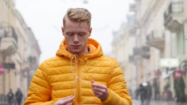 Retrato de un joven con auriculares mientras camina por la calle de invierno de la ciudad y comienza a escuchar música — Vídeo de stock