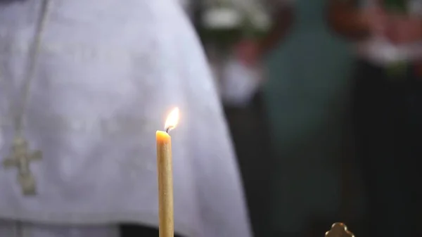 Die Kerze brennt in einer Kirche. Priester im Hintergrund. Selektiver Fokus — Stockfoto