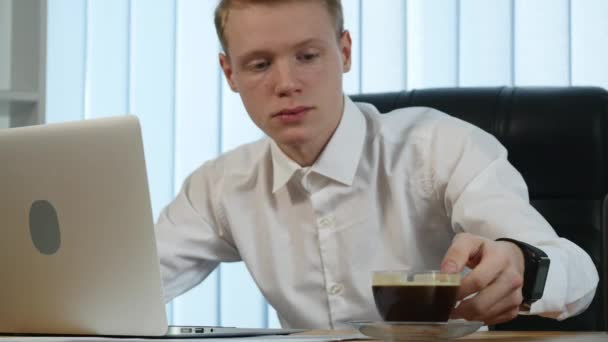 Zakenman werkzaam bij Bureau met zijn laptop en het drinken van koffie, omringd door een heleboel papierwerk en financiële verslagen — Stockvideo