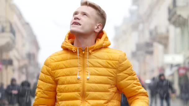 Retrato de um jovem usando fones de ouvido enquanto caminha na rua de inverno na cidade e começa a ouvir música — Vídeo de Stock