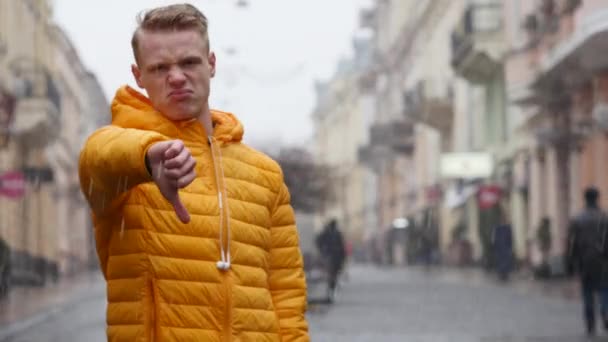 Hombre sonriente en la calle muestra los pulgares hacia abajo. la nieve cae en el fondo — Vídeos de Stock