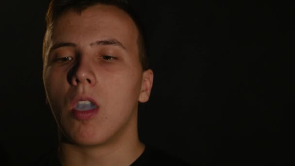 Человек, курящий электронный сигаретный пар на черном фоне — стоковое видео