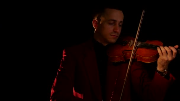 Um jovem de fato vermelho toca violino num fundo preto. — Vídeo de Stock