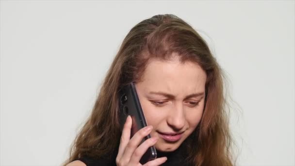 Mujer joven enojada hablando en su teléfono celular sobre un fondo blanco — Vídeo de stock