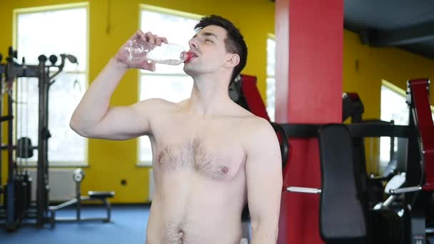 Hombre atlético adulto joven en ropa deportiva hidratante de una botella de agua de plástico de color en el gimnasio durante un descanso de entrenamiento crossfit — Vídeo de stock