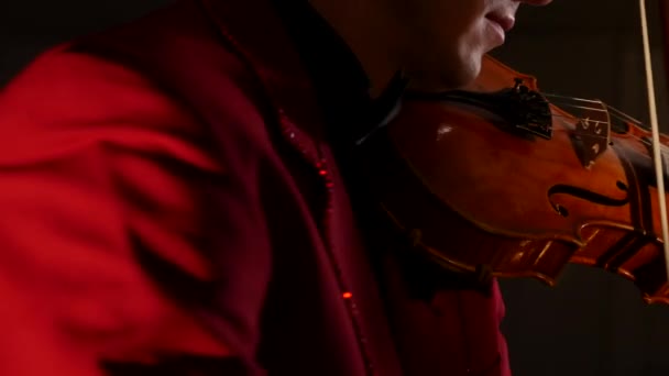 Mladý muž v červeném obleku hraje na housle na černém pozadí — Stock video
