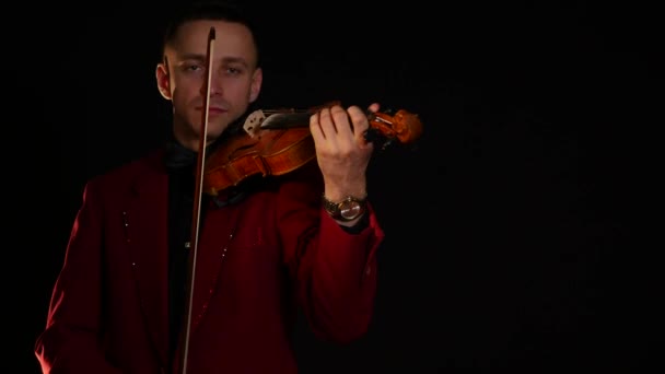 Mladý muž v červeném obleku hraje na housle na černém pozadí — Stock video