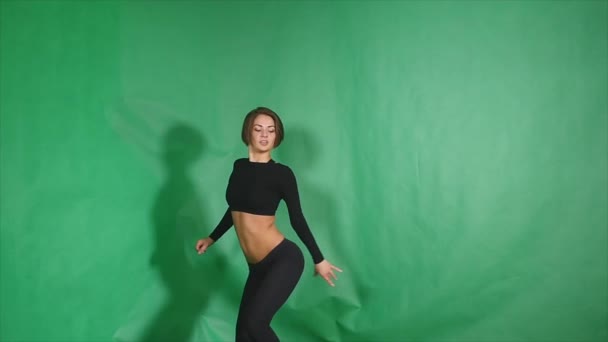 Сексуальная девушка делает элемент в танце на шесте на зеленом фоне — стоковое видео