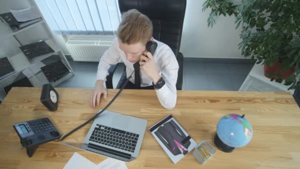 Młody człowiek w garniturze, siedząc w biurze, mówiąc na telefon. Pracujesz w koncepcji pakietu office. Widok z góry — Wideo stockowe