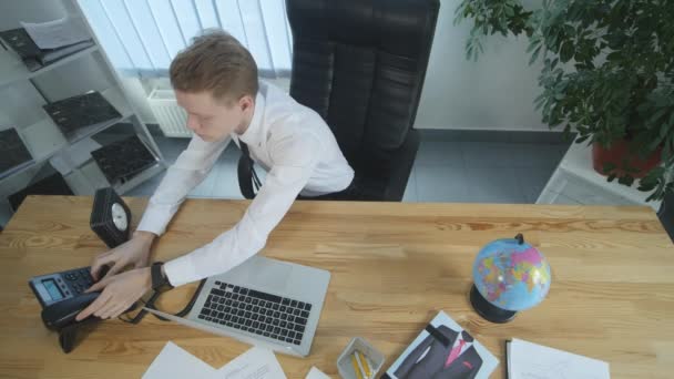 Un joven con traje sentado en la oficina, hablando por teléfono. Trabajar en el concepto de oficina. vista superior — Vídeos de Stock