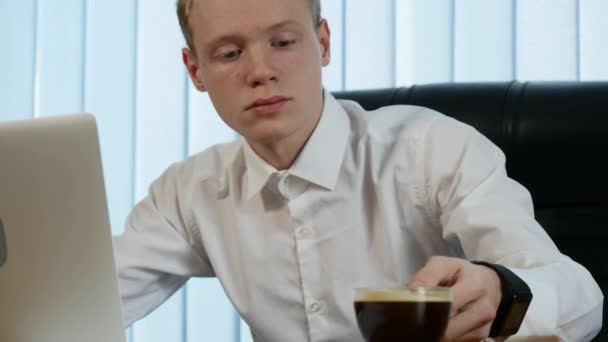 Zakenman werkzaam bij Bureau met zijn laptop en het drinken van koffie, omringd door een heleboel papierwerk en financiële verslagen — Stockvideo