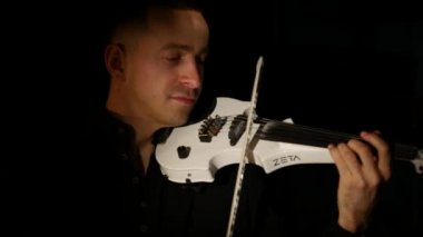 Kemancı adam siyah bir arka planda keman çalıyor. Yakın çekim