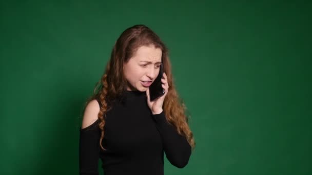 Arg ung kvinna talar i hennes mobiltelefon på en grön bakgrund — Stockvideo
