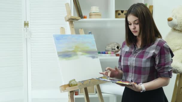Jonge vrouw kunstenaar in schort schilderij foto op canvas in art studio — Stockvideo