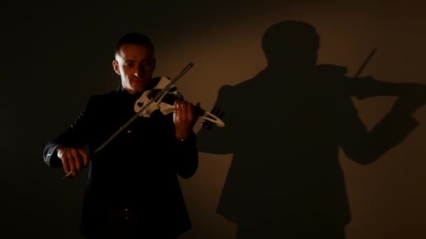 Молодой человек играет на скрипке в темной комнате — стоковое видео